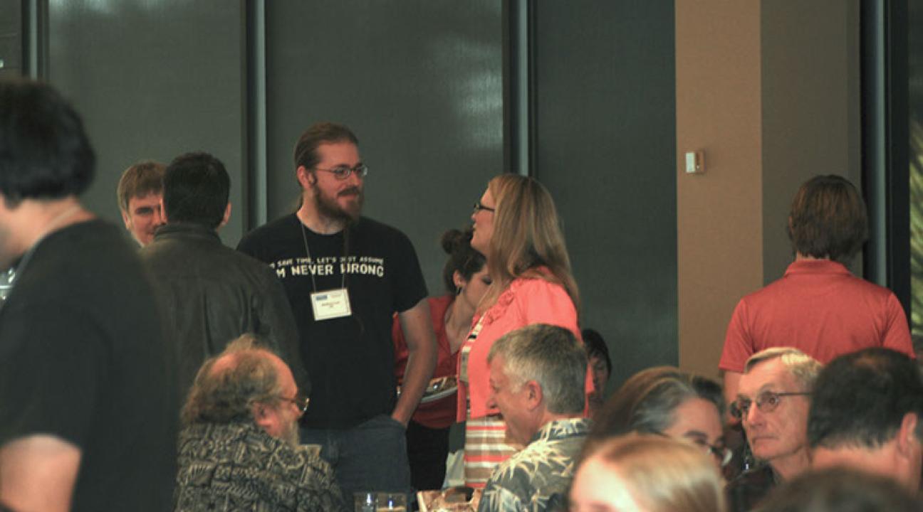 Two people standing in a crowded room, talking nearby seated people