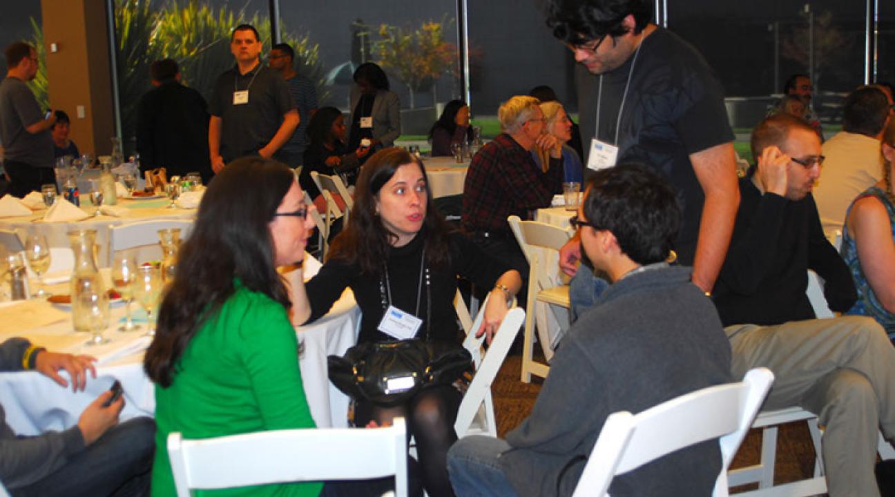 Three people sitting at a table in a crowded room, talking excitedly