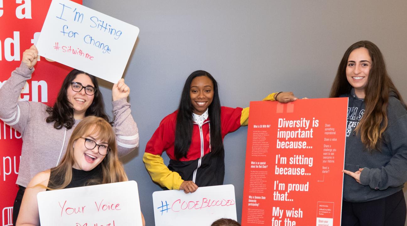 Five women holding up signs with #SitWithMe messages, posing while standing and sitting in the RedChair