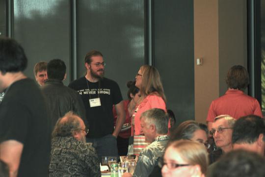Two people standing in a crowded room, talking nearby seated people