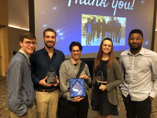 Five students posing, holding three crystal awards