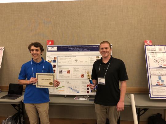 Two students receiving an award, posing in front of a research poster